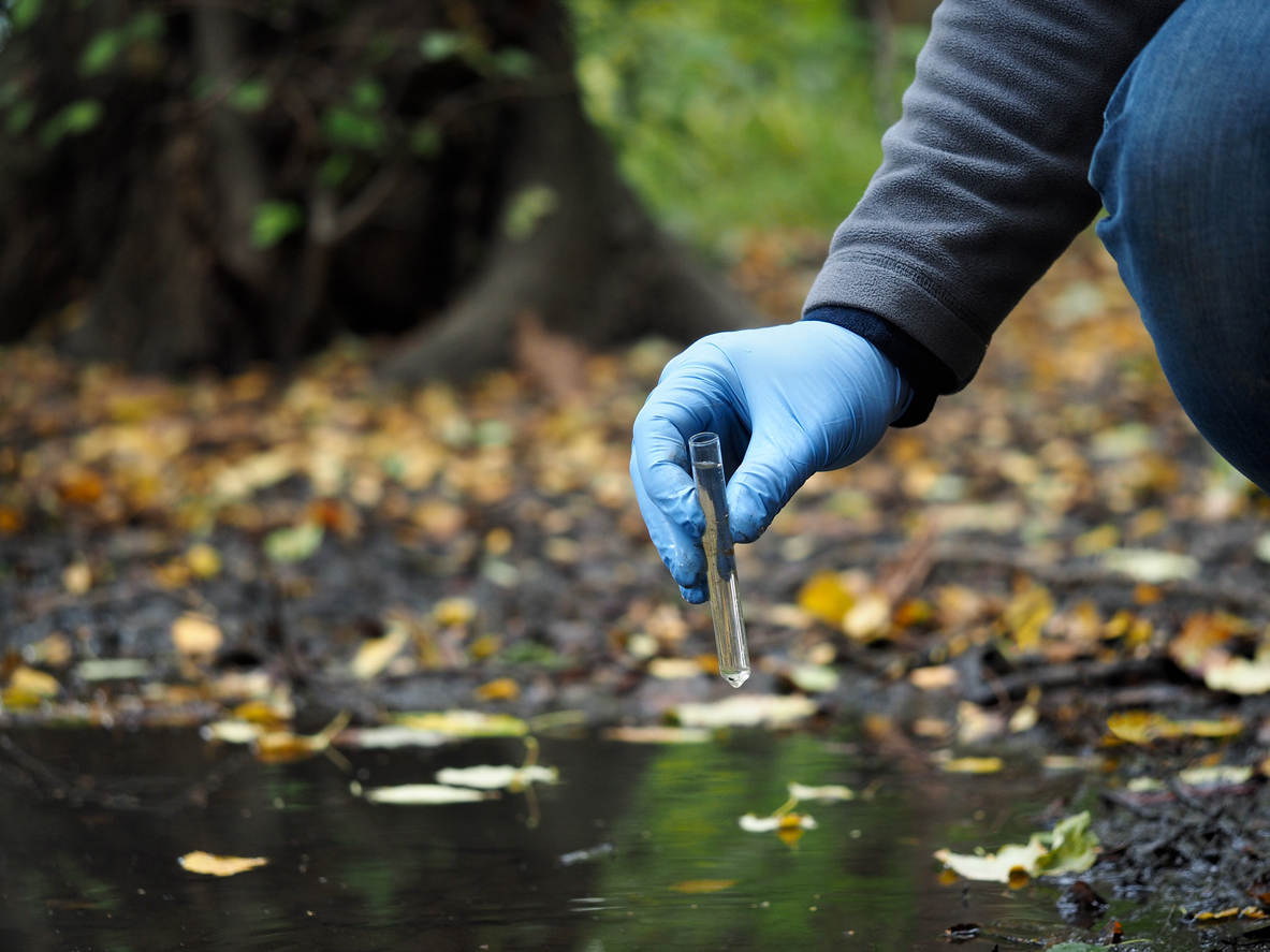 Water sample. Hand in glove collects water from a puddle in a test tube. Analysis of water purity, environment, ecology - concept. Water testing for infections, harmful emissions